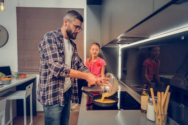 Tall dark-haired bebaarde man in een geruit hemd koken omelet — Stockfoto