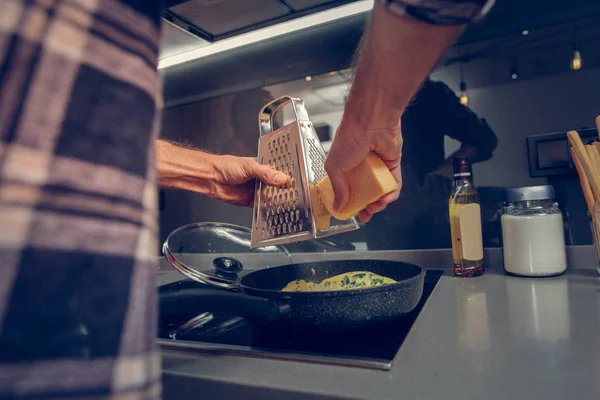 Homem alto em uma camisa quadriculada ralando queijo na omelete — Fotografia de Stock