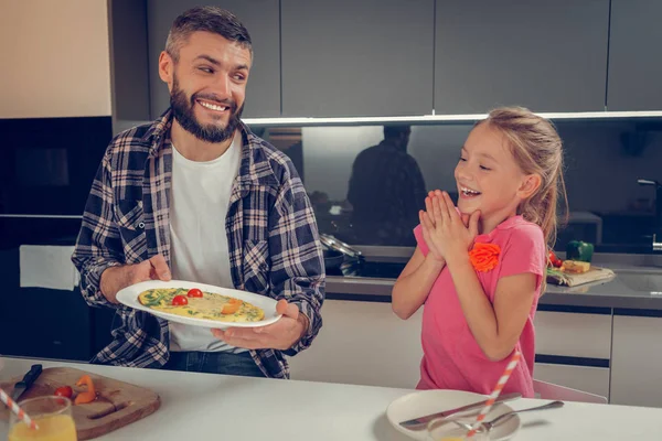 Bebaarde tall man in een geruite shirt klaar omelet tonen aan zijn dochter — Stockfoto