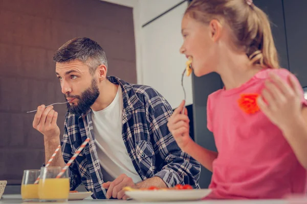 Söta ljushårig flicka i en rosa t-shirt och hennes far som äter omelett — Stockfoto