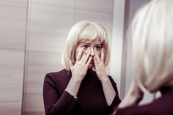 Worried blonde girl wiping tears from eyes
