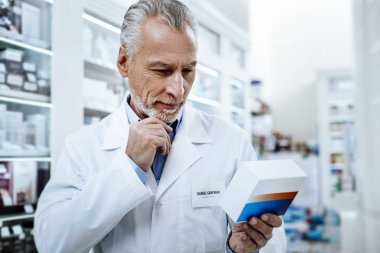 Memnun seyir beyaz önlük ve sakallı güneş yanığı gri saçlı eczacı