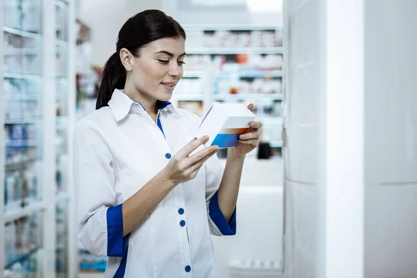 Belle jeune femme aux cheveux bruns dans un manteau blanc scrutant le nouveau médicament — Photo