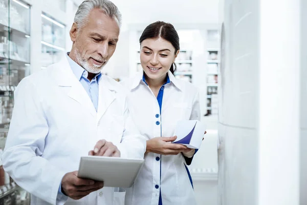 Director de una farmacia con una bata blanca explicando el material a su nuevo colega — Foto de Stock