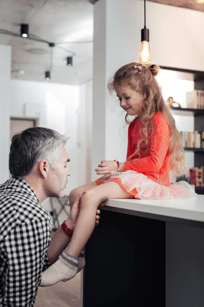 Padre alto dai capelli grigi con una camicia a scacchi che guarda il ginocchio ferito — Foto Stock