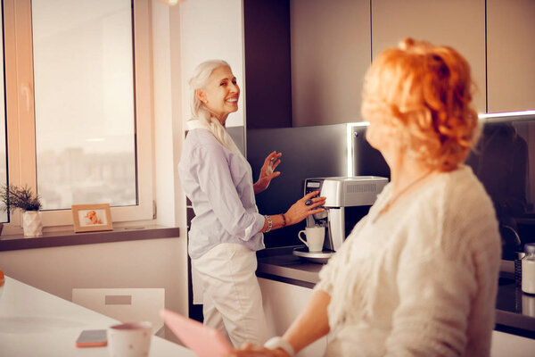 Positive senior woman standing near the coffee machine