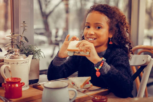 Grappige leuk krullend meisje bijten haar smakelijke sandwich met groenten — Stockfoto