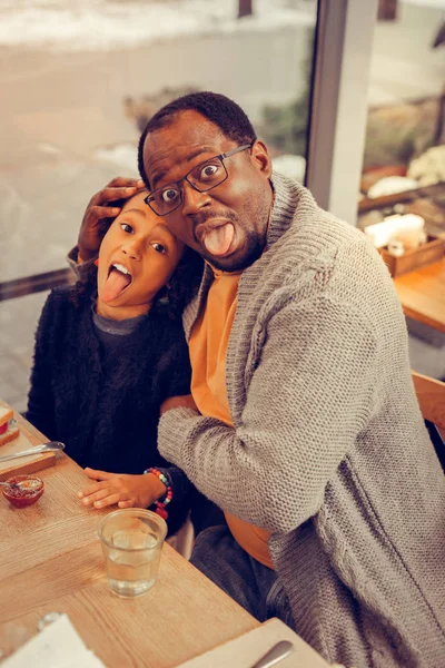 Pai e filha fazendo caras engraçadas enquanto toma café da manhã na cafetaria — Fotografia de Stock