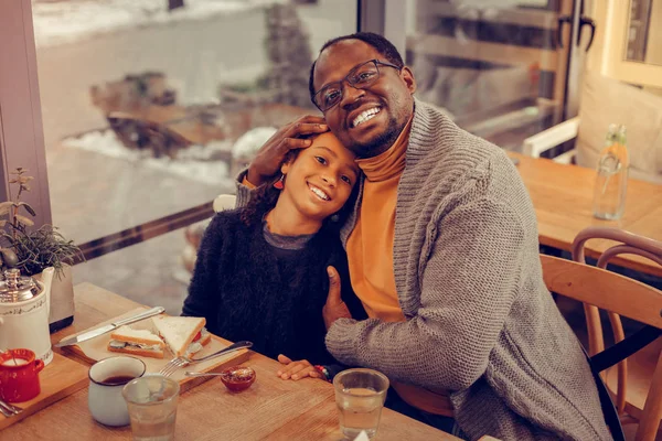 Cheerful dark-haired father wearing glasses hugging his cute girl — Stock Photo, Image