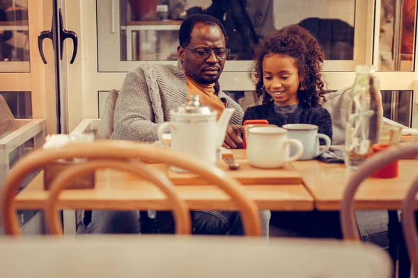 Father and daughter playing game on smartphone sitting in cafeteria — Stock Photo, Image