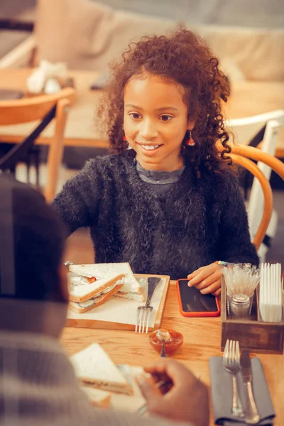 Mooie aansprekende krullend dochter eten boterham zitten in cafetaria — Stockfoto