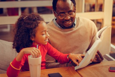 Kıvırcık siyah saçlı kızı babası ile kitap okuma Bilezik takıyor