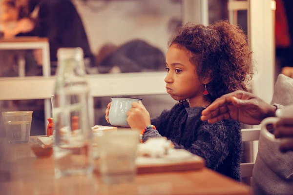 Mooi krullend meisje dragen blauwe trui het drinken van thee in cafetaria — Stockfoto