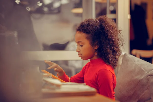 Curly dark-haired girl feeling involved in playing game on tablet — Stock Photo, Image