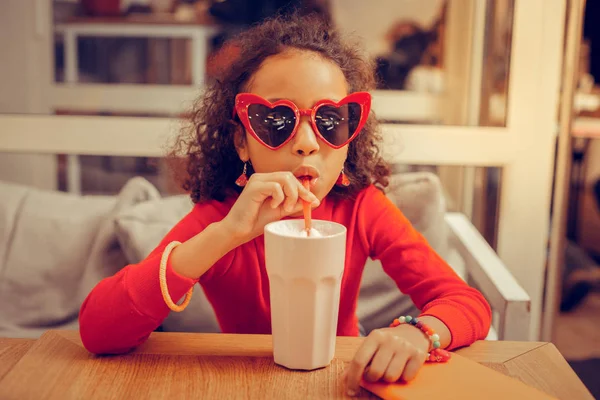 Elegantní dívka, která nosí červený rolák a sluneční brýle sedí v kavárně — Stock fotografie