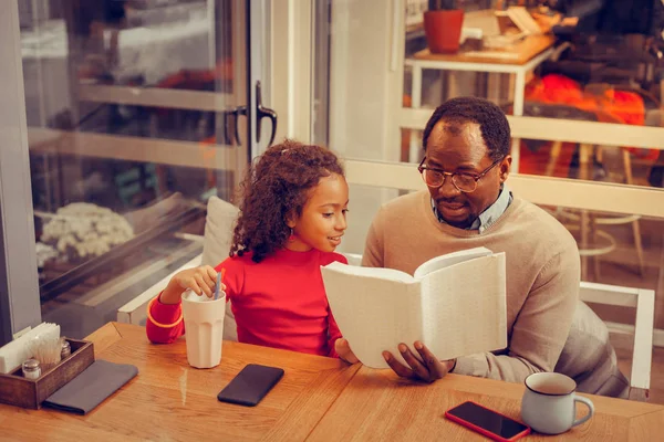 Piccola ragazza riccia che ascolta suo padre leggere il libro per lei — Foto Stock