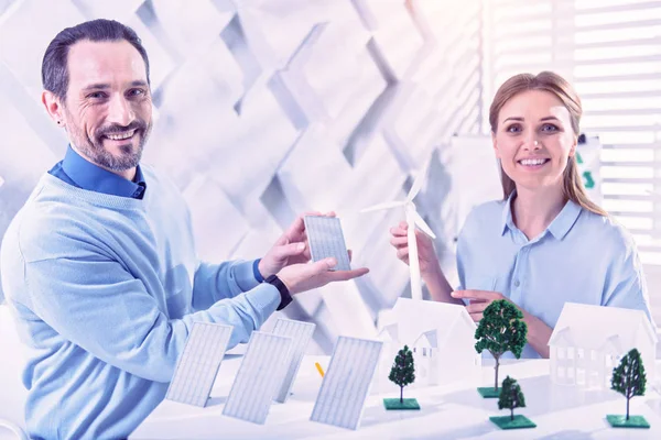 Happy eco engineers showing solar batteries and windmill turbines — Stock Photo, Image