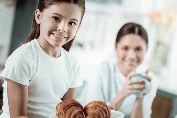 Linda colegiala comiendo sabrosos croissants en la cocina —  Fotos de Stock