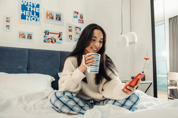 Mujer sosteniendo su teléfono inteligente rojo mientras lee las noticias — Foto de Stock