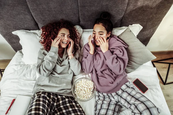 Novias con pijama acostadas en la cama con palomitas de maíz — Foto de Stock