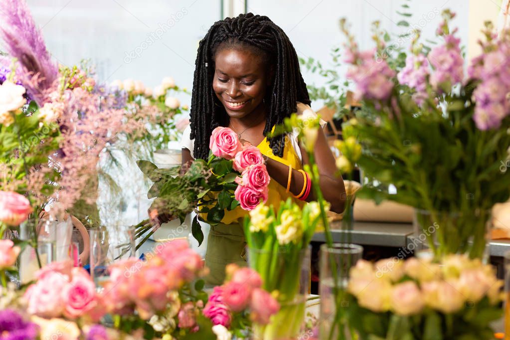 Good choice. Beautiful dark-skinned woman keeping smile on her face while looking at flowers
