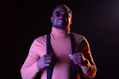 Bana katıl. Jartiyer tutarak siyah duvardan ayakta neşeli esmer erkek kişi