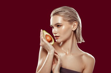 Blonde-haired model holding avocado near her face while working clipart