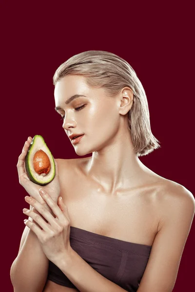 Blonde-haired model wearing dark top holding avocado — Stock Photo, Image