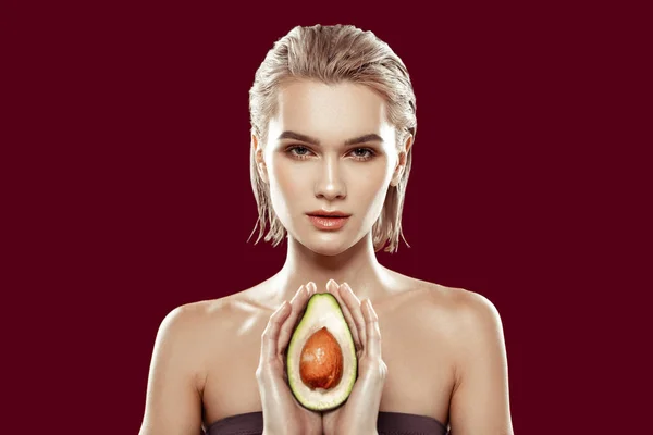 Model holding avocado in her hands standing near red wall — Stock Photo, Image