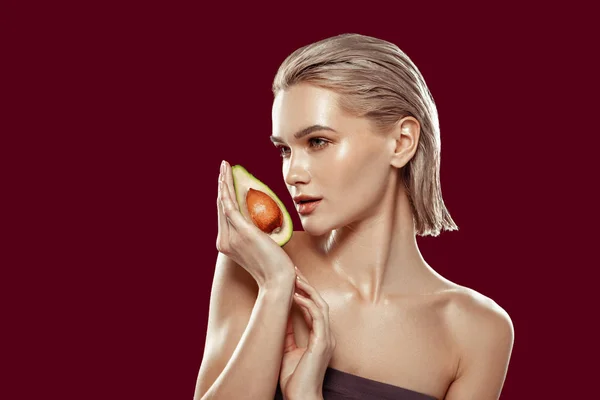Blonde-haired model holding avocado near her face while working