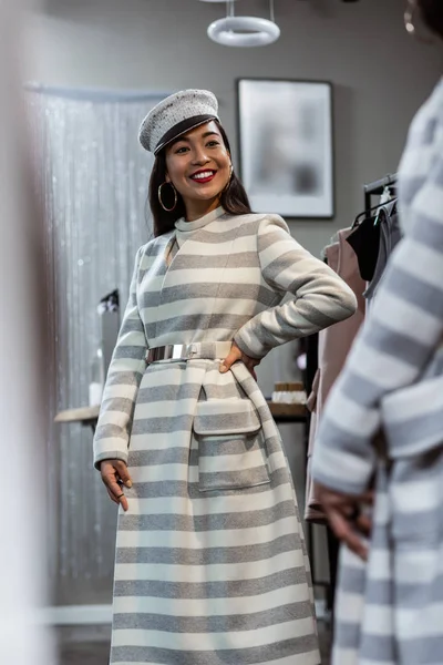 Молодая азиатская сияющая женщина в полосатом пальто выглядит счастливой — стоковое фото
