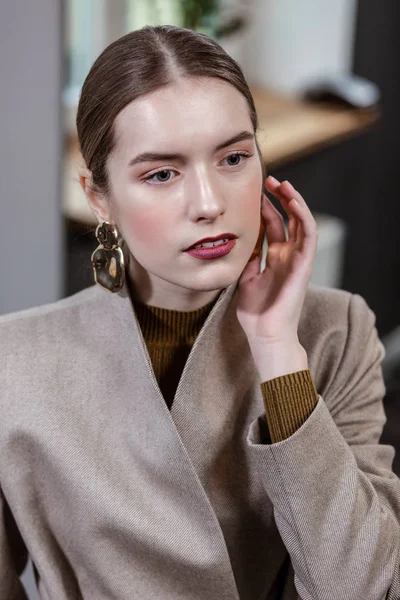 Schöne langhaarige hübsche Frau in einer stylischen Jacke, die ihren Ohrring berührt — Stockfoto