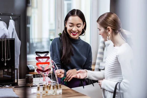 Dark-haired lachende Aziatische vrouw in een Marine polo nek testen van een nieuwe parfum — Stockfoto