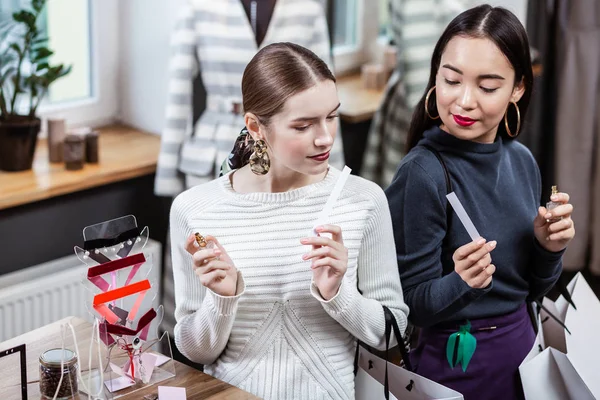 Lachende vrij langharige vrouw in een witte trui genieten van een nieuw parfum — Stockfoto