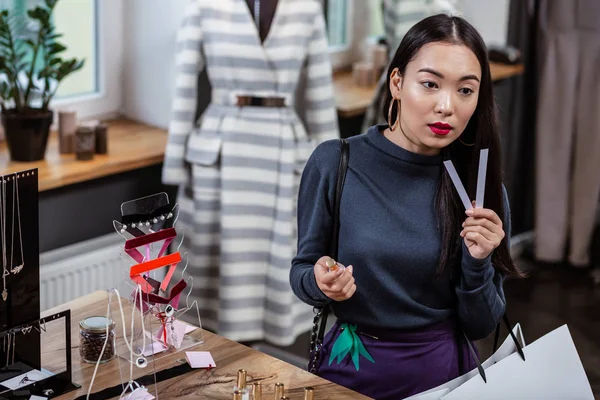 Dark-haired smiling asian lady in a dark-blue blouse smelling a perfume — Stock Photo, Image