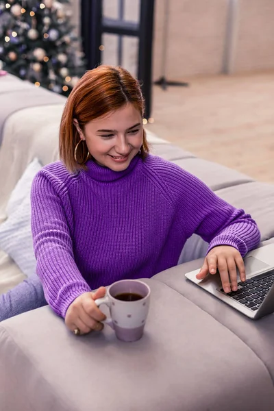 Bastante joven pelirroja radiante chica en un suéter violeta charlando con amigos en Internet — Foto de Stock