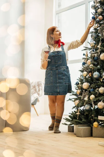 Hermosa chica pelirroja con grandes pendientes tocando el adorno del árbol de Navidad — Foto de Stock