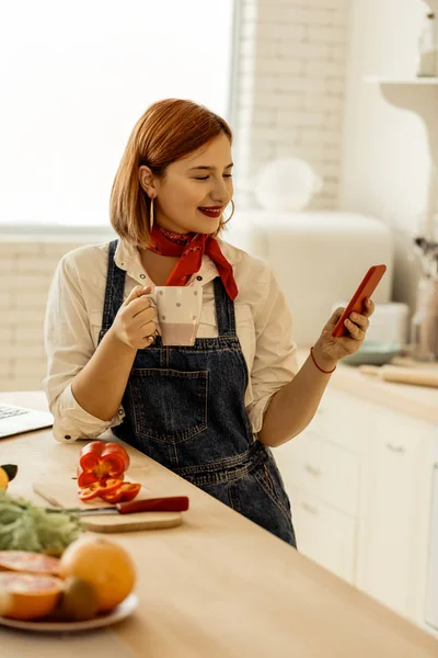 Рыжая девушка с пирсингом в носу держит телефон в руках — стоковое фото