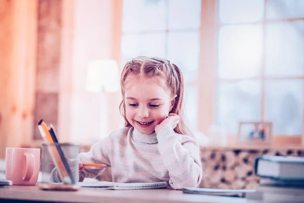 Весела маленька дівчинка відчуває себе щасливою, роблячи домашнє завдання — стокове фото