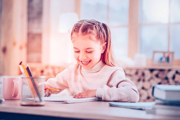Adorable young schoolgirl smiling while drawing in her album — Stock Photo, Image