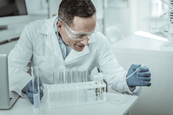 Smiling contented researcher sitting against whole set of special equipment