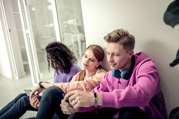 Estudiante guapo usando reloj inteligente usando su teléfono inteligente — Foto de Stock