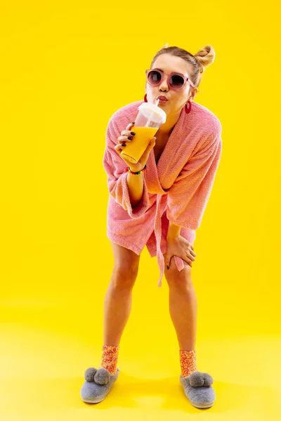 Mujer joven que usa albornoz y jugo de casa bebiendo jugo — Foto de Stock