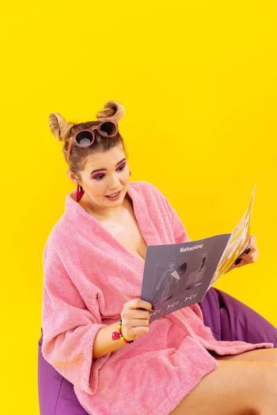 Wanita muda mengenakan jubah mandi merah muda membaca majalah modern — Stok Foto