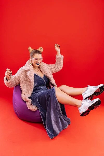 Mujer vistiendo abrigo y zapatillas de deporte cayendo en la silla beanbag —  Fotos de Stock