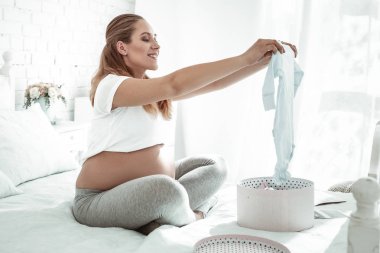 Yatağın üstüne oturan ve mavi romper getiren aktif kadın