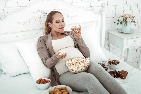 Dicke, erwartungsvolle Frau in Pastellkostüm liegt im Bett und trägt Donut — Stockfoto