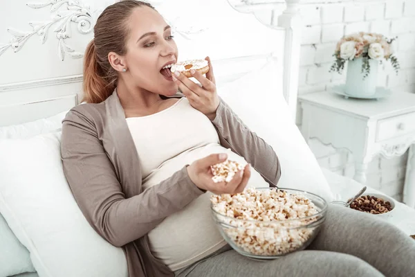 Schwangere attraktive Dame mit langem Pferdeschwanz beißt glasierten Donut — Stockfoto