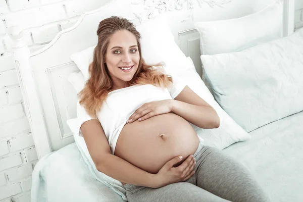Приятная женщина с широкой улыбкой, завернутая в живот беременной — стоковое фото