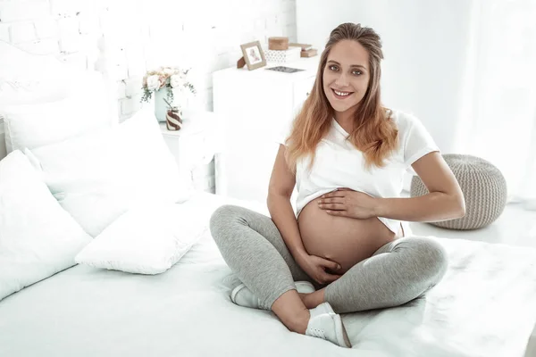 Smiling future mother lifting her t-shirt and presenting round stomach — Stock Photo, Image